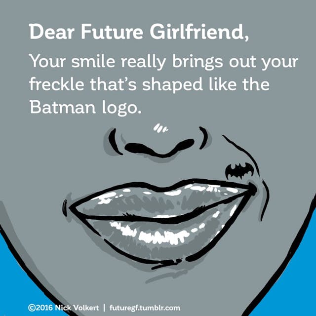 A woman smiles with a beauty mark that is in the shape of the batman logo.